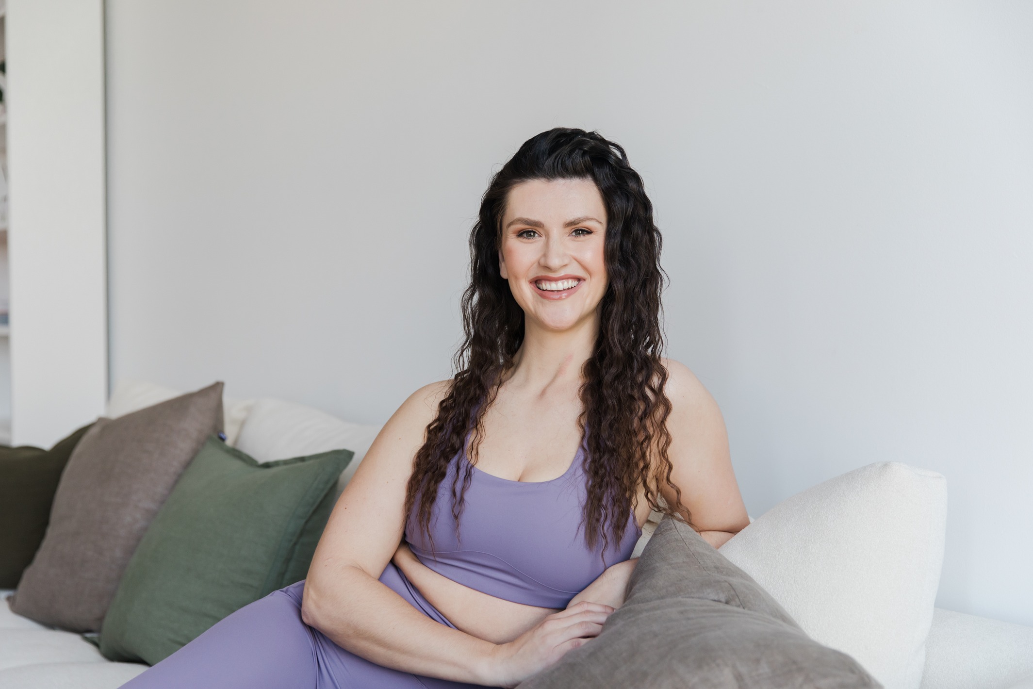 Hailey Ann Co Bookkeeper & Somatic Money Coach for Female Entrepreneurs sitting on a couch smiling. Professional Headshot